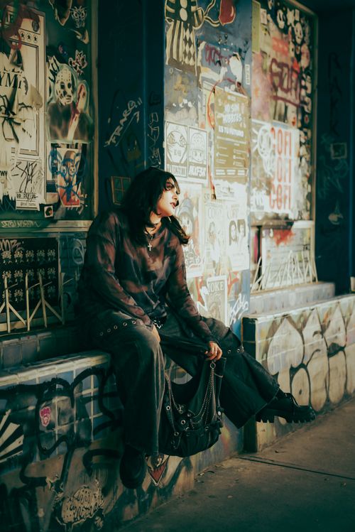Free Young adult in urban setting sitting against graffiti-covered wall, showcasing street style. Stock Photo