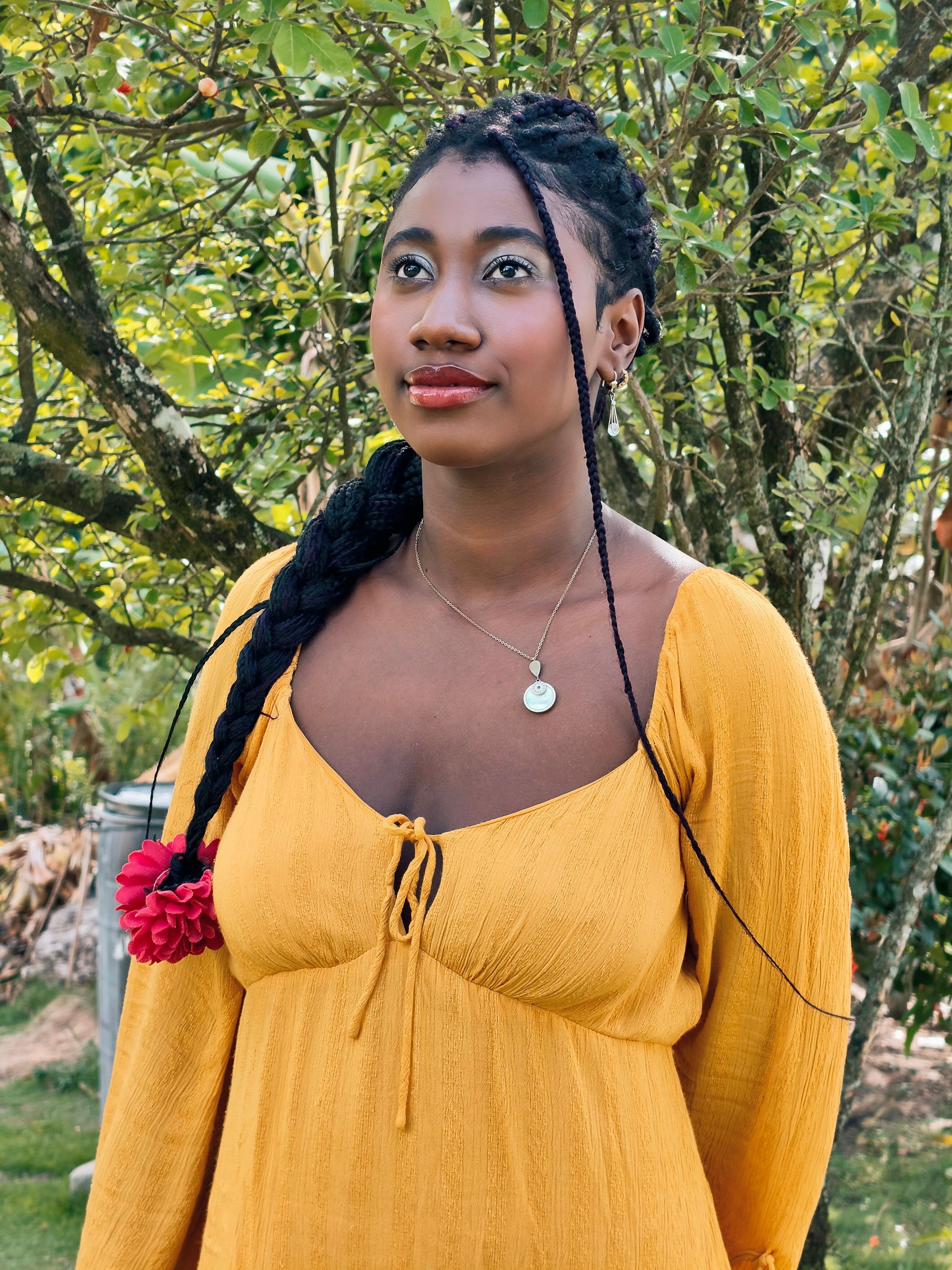 A woman in a yellow dress stands among trees, exuding warmth and elegance.