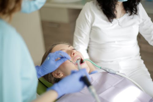 From above of crop dentist and assistant in mask and gloves curing teeth of young female patient in modern clinic