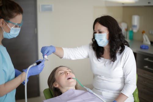 Middle aged female lying in dental chair with tube suction in mouth while getting professional treatment to fill cavity in tooth in dental clinic