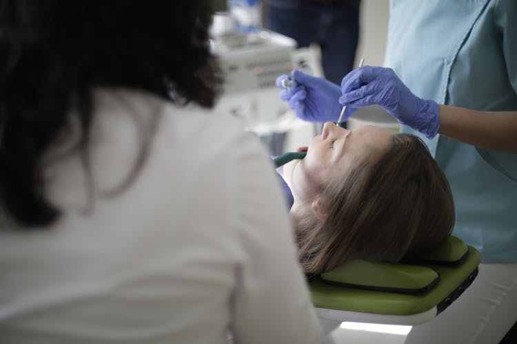 Faceless Female Dentist Using Drill And Mouth Mirror While Curing Teeth Of Patient