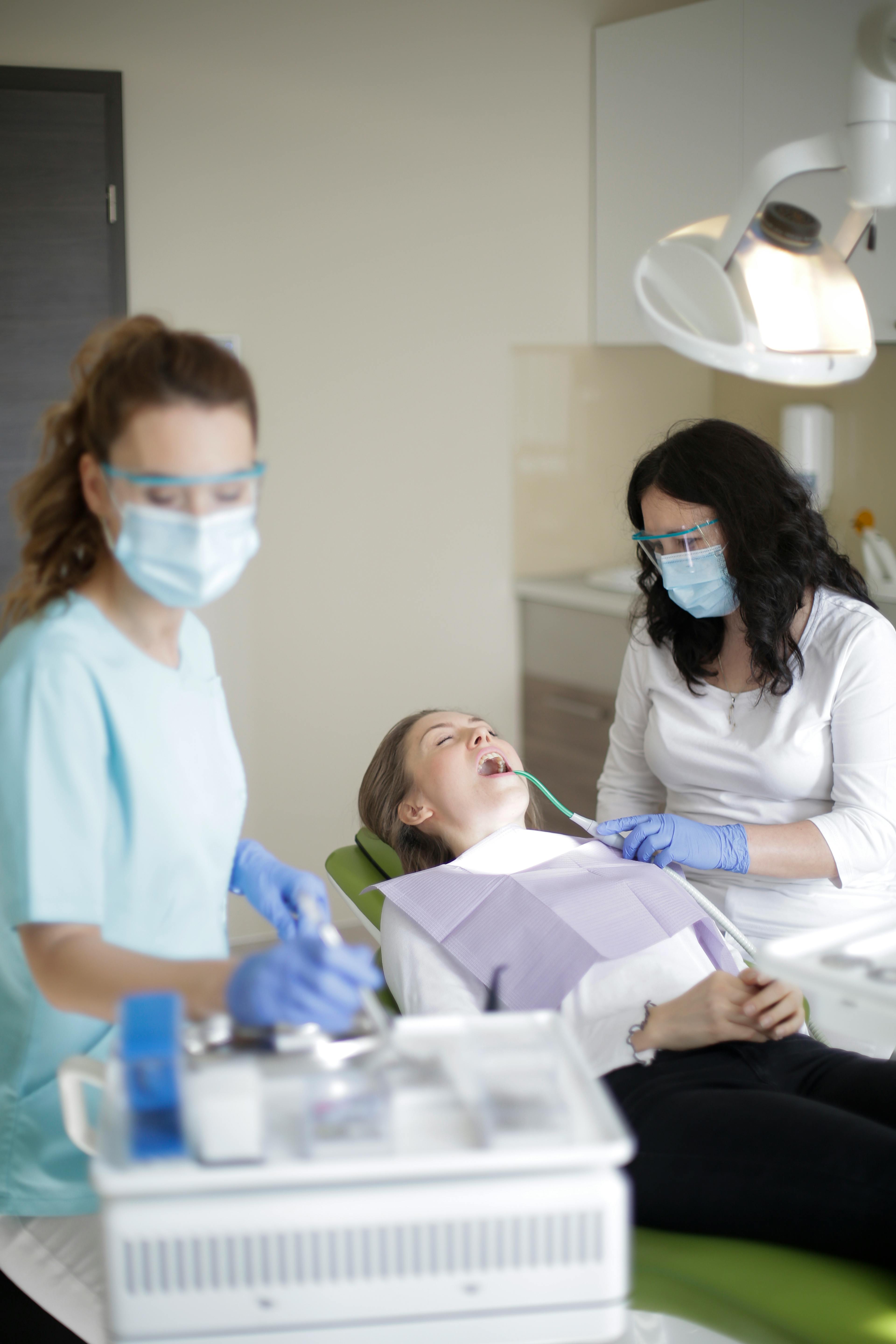 female dentist with assistant using dental tools and equipment while curing teeth of patient