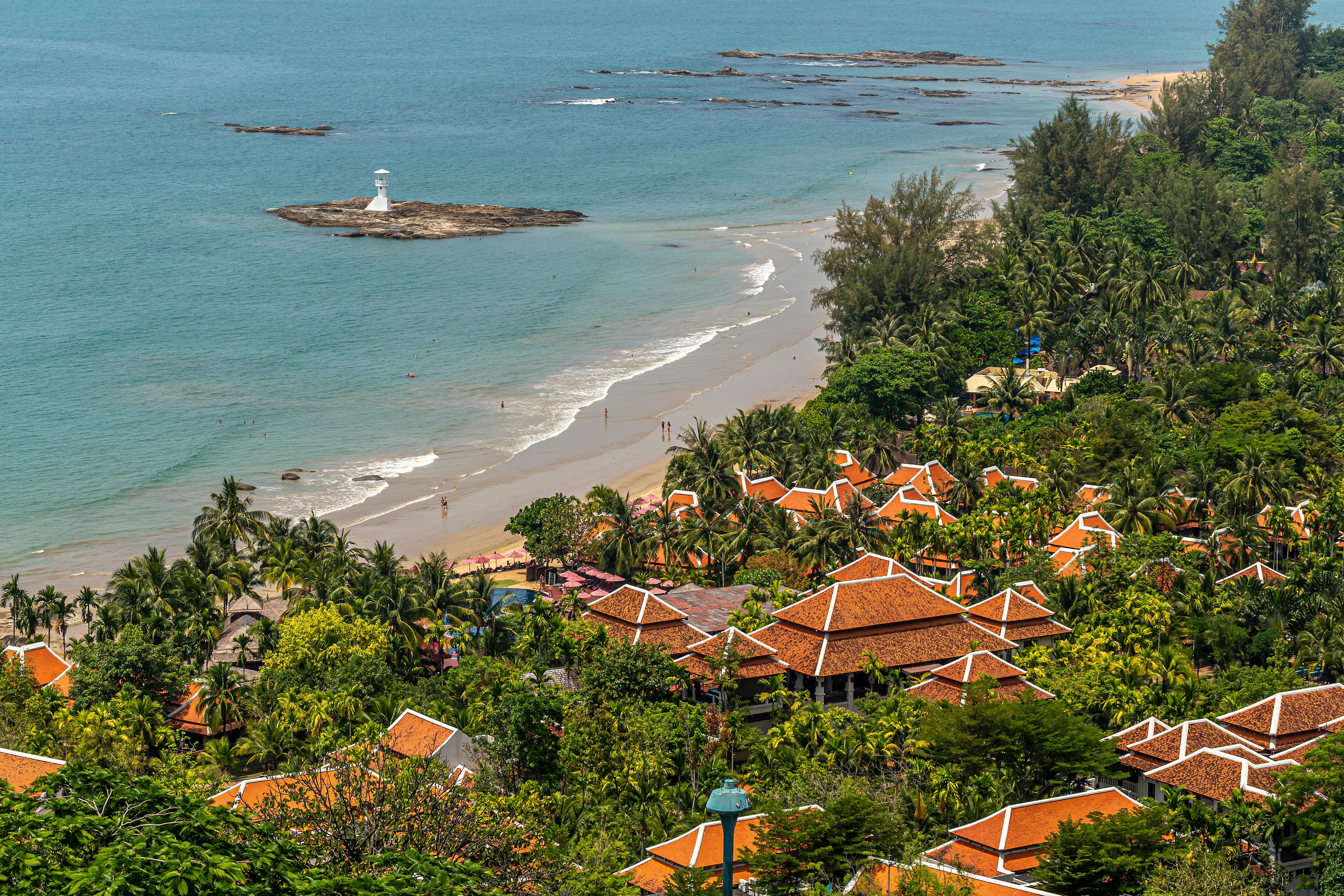 Free A picturesque beachfront village with terracotta roofs, palm trees, and a distant lighthouse. Stock Photo