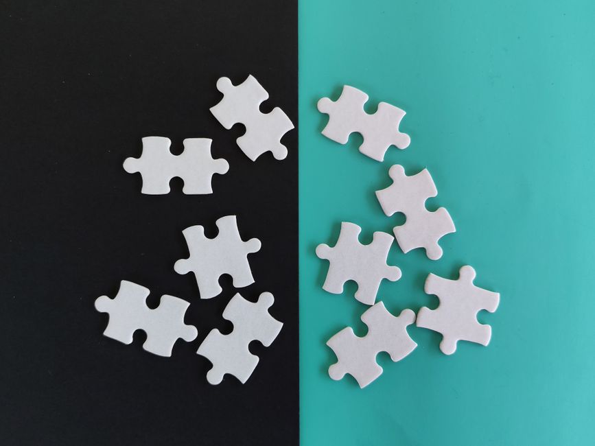 White puzzle pieces arranged on a contrasting black and teal background, symbolizing duality.