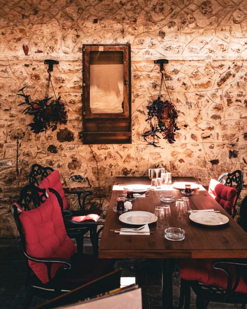 Free Inviting outdoor dining space with rustic stonework, set for a gathering with colorful chairs and warm sunlight. Stock Photo
