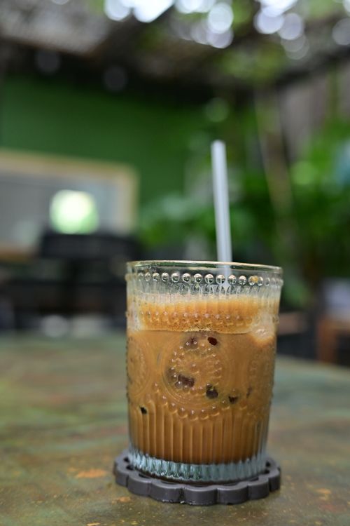 Free Close-up of an iced coffee in a decorative glass with straw on a rustic outdoor table. Stock Photo
