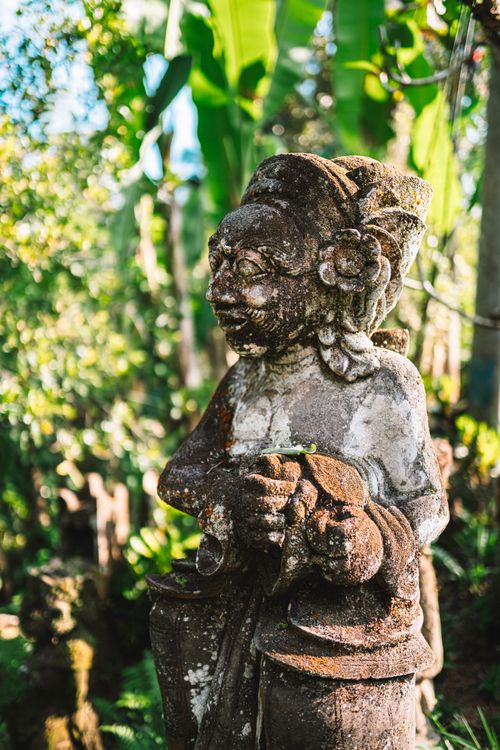 Free A weathered stone statue amidst lush greenery in a Balinese tropical garden, showcasing traditional Balinese artistry. Stock Photo