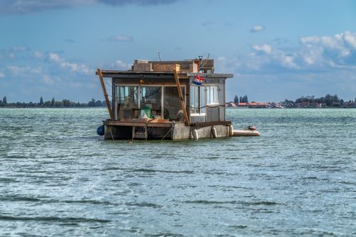 Free Scenic view of a houseboat floating on tranquil waters with a distant shoreline under a blue sky. Stock Photo