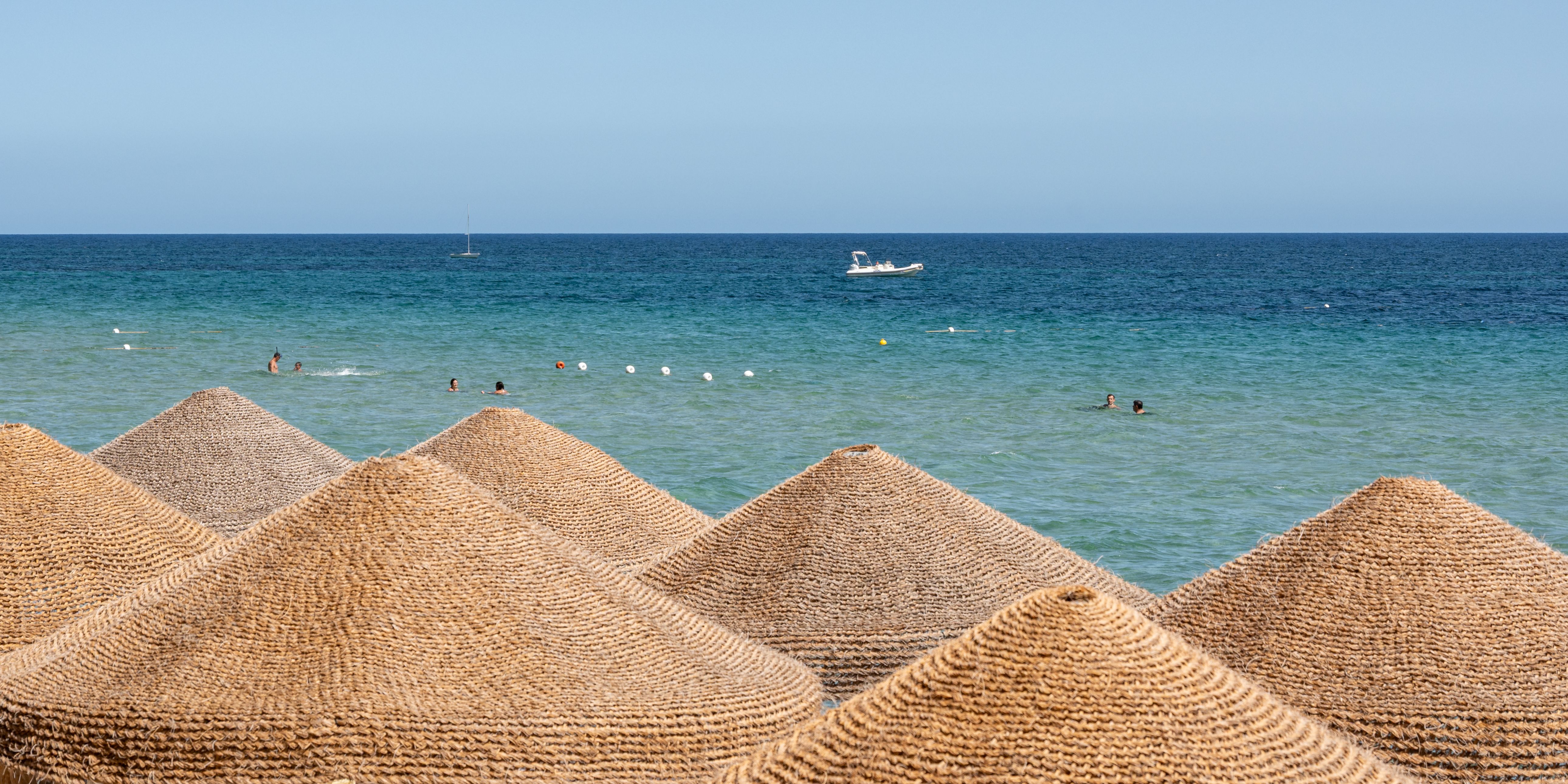 Wicker beach umbrellas overlook a tranquil sea at Santa Margherita di Pula, Sardinia.