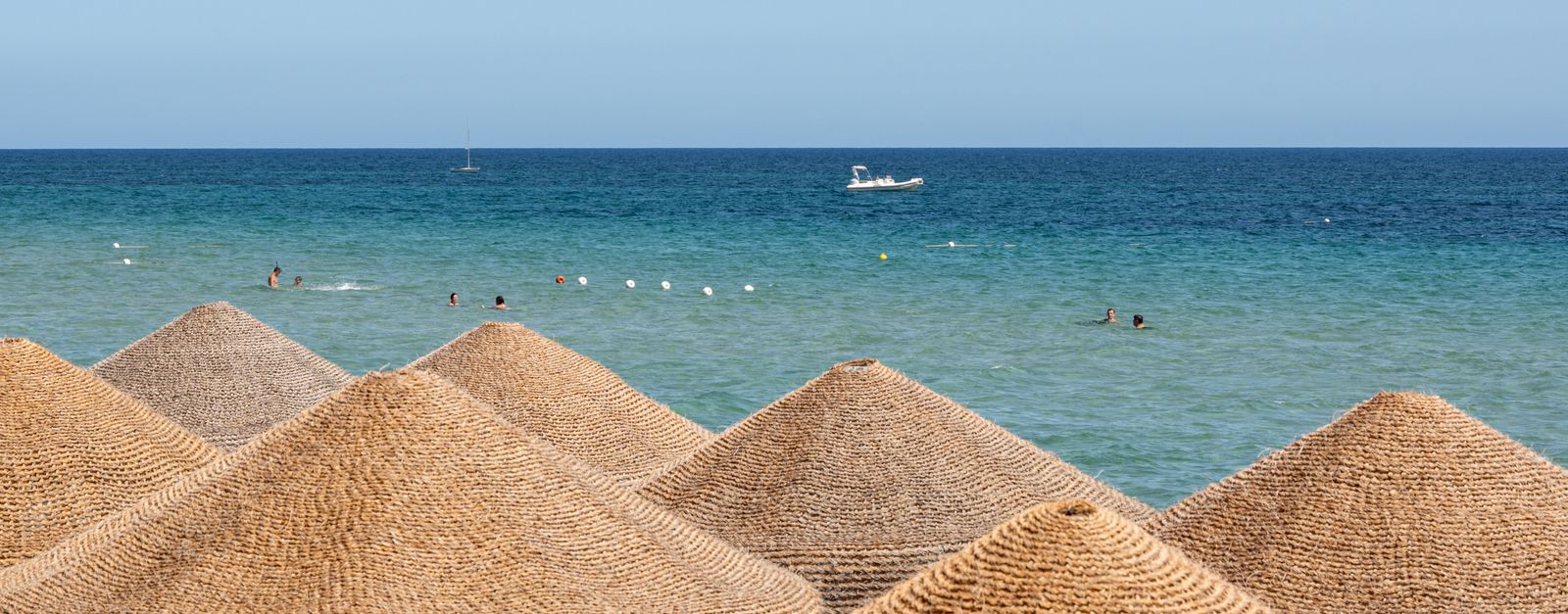 Wicker beach umbrellas overlook a tranquil sea at Santa Margherita di Pula, Sardinia.