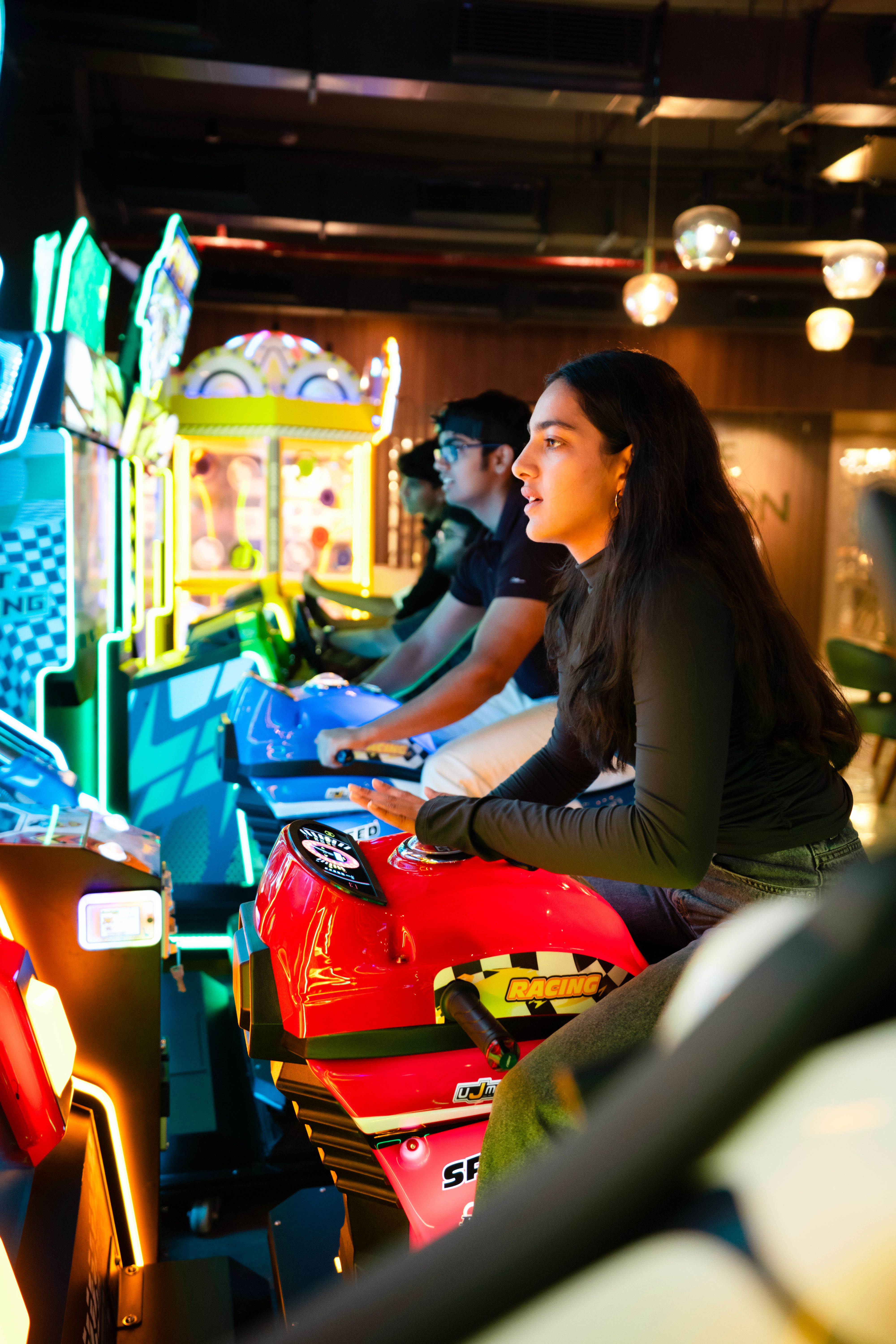 Young adults engaged in an arcade racing game experience, vibrant neon lights.