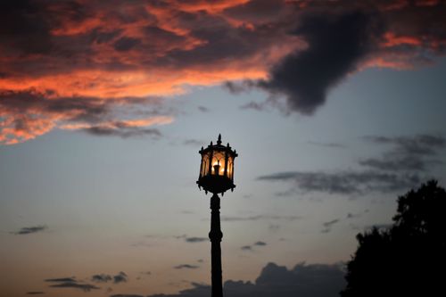 Free A lone street lamp silhouetted against a dramatic sunset sky with vivid clouds enhancing the scene. Stock Photo