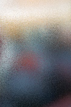 Defocused backdrop of translucent glass with spots of bright colors glowing through window on blurred background in daylight in room
