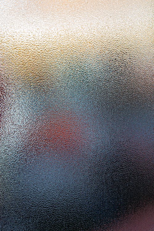 Defocused backdrop of translucent glass with spots of bright colors glowing through window on blurred background in daylight in room