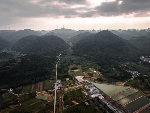 Free Scenic aerial view of lush hills, wind turbines, and fields under cloudy sky. Stock Photo