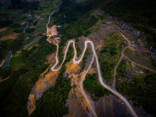 Free Aerial view of a winding mountain road surrounded by lush greenery and farmland at sunset. Stock Photo