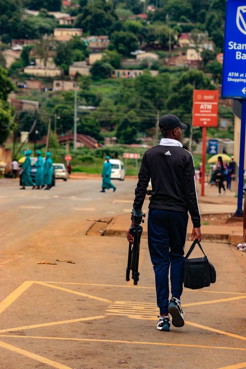 Free A man walks down the street in Piggs Peak, Eswatini, carrying photography equipment. Stock Photo