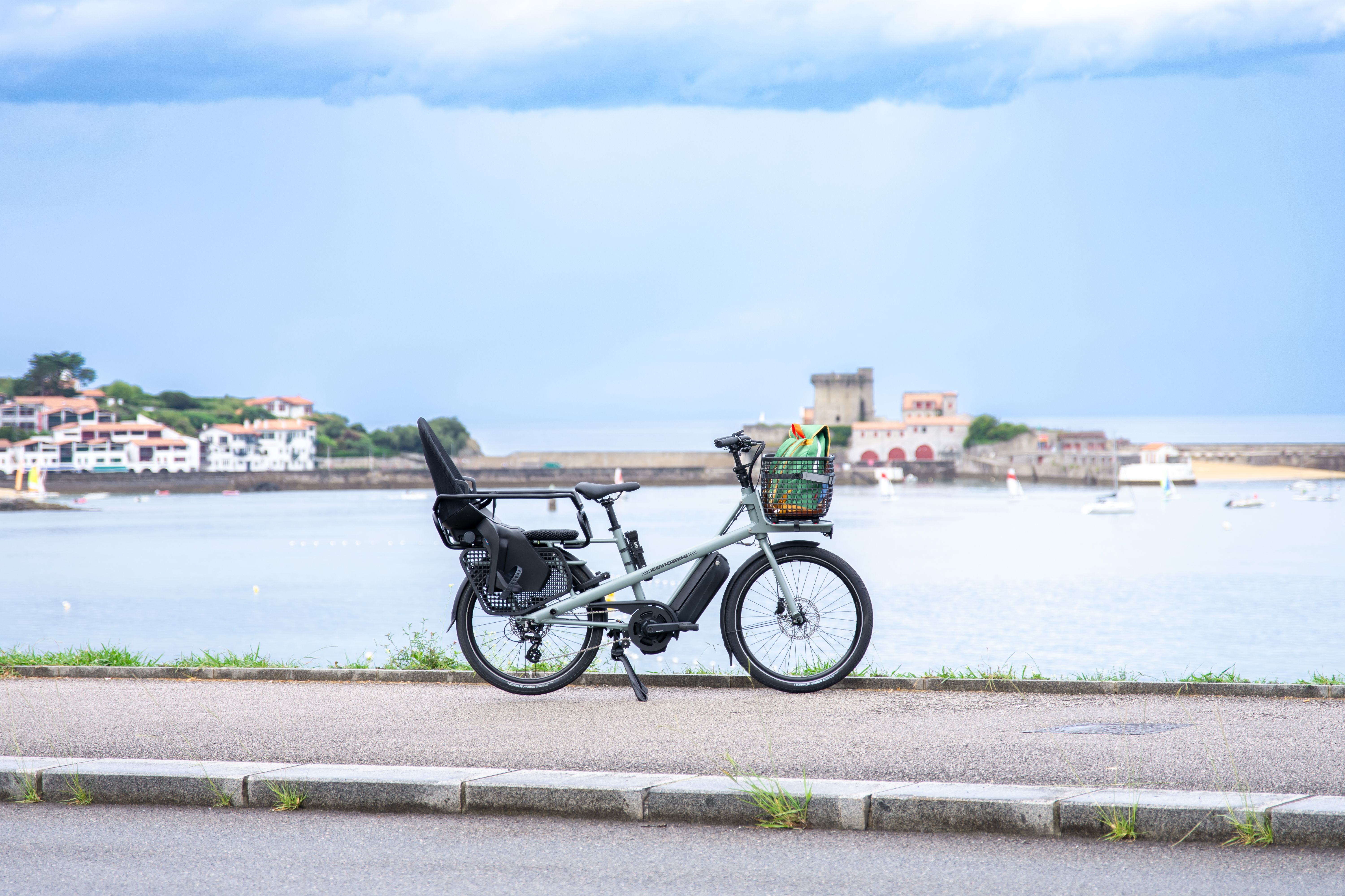 Electric cargo bike by a waterfront in Saint-Jean-de-Luz, France, under a cloudy sky.