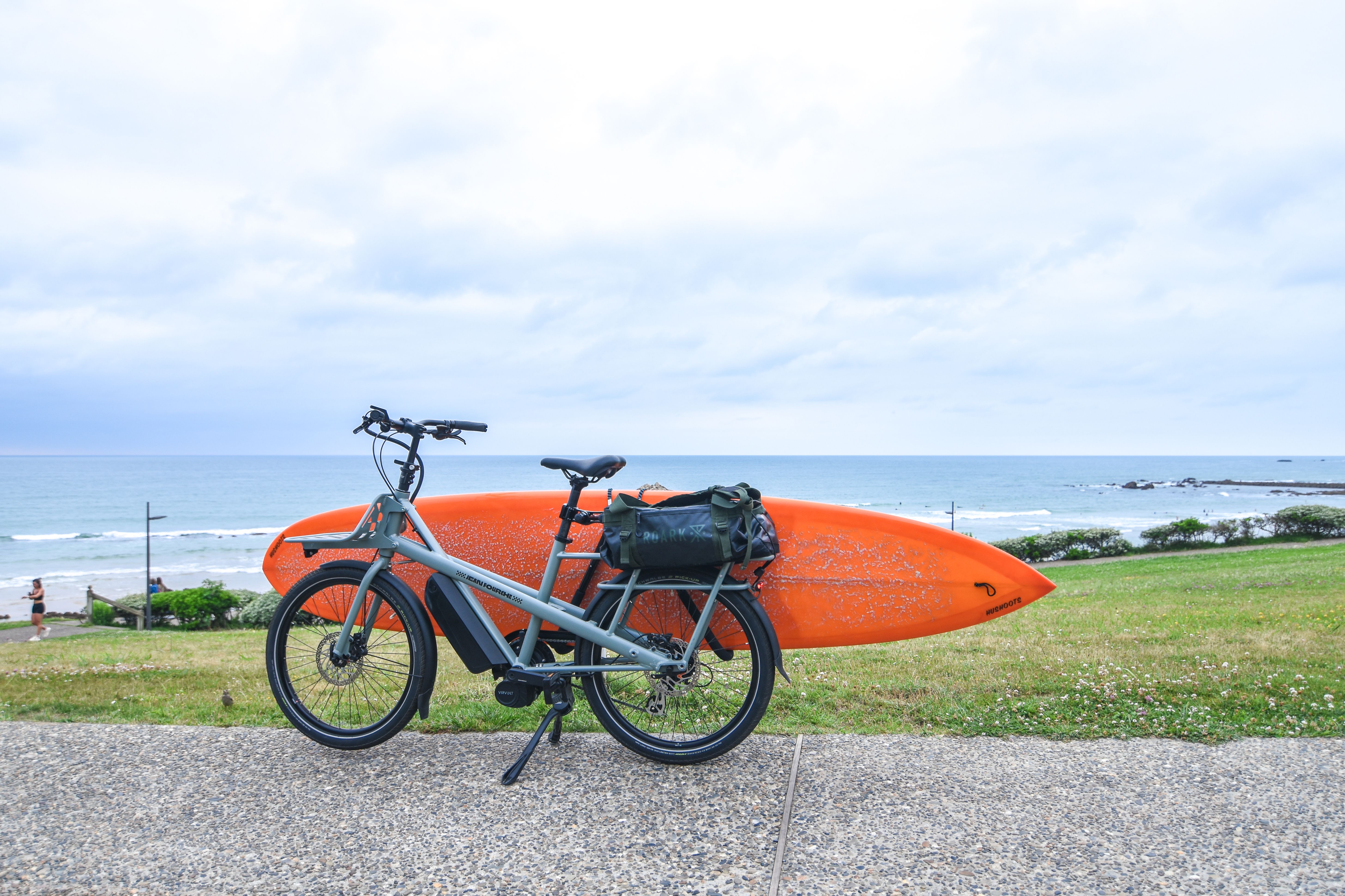 E-bike parked on a coastal road in Biarritz with an orange surfboard mounted on it.