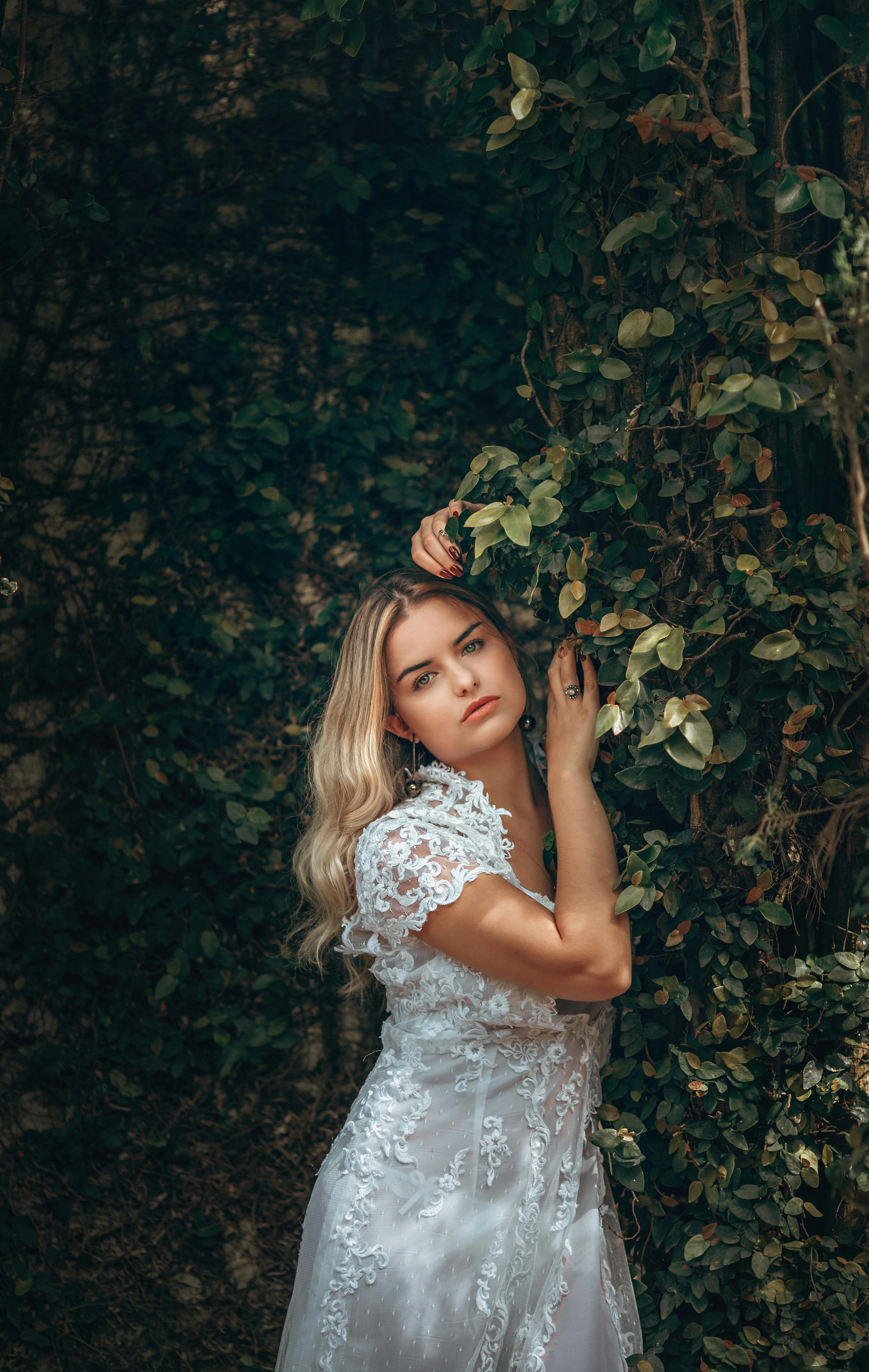 Beautiful woman in a white lace dress posing amidst lush green leaves. Natural elegance and fashion portrait.