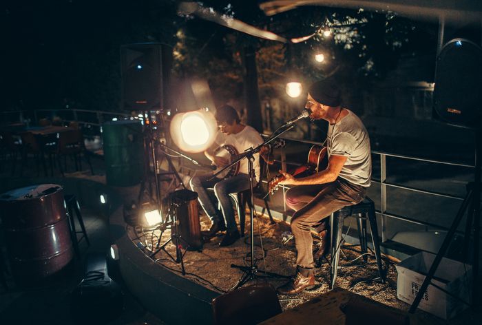 Two musicians playing acoustic guitar outdoors at night — photo by Helena Lopes on Pexels