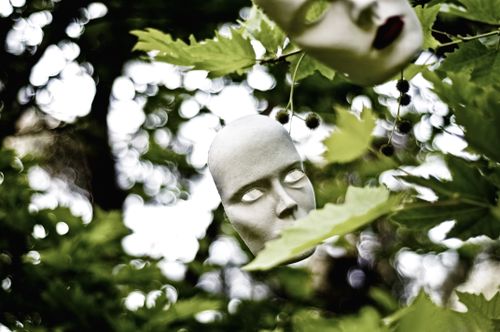 Free Eerie white masks suspended among vibrant green leaves in a forest setting. Stock Photo