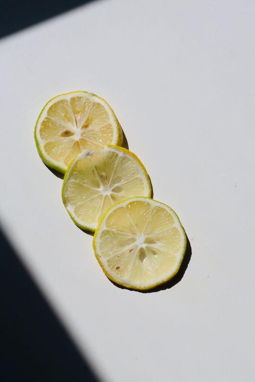 Free Three lemon slices on white background with dramatic shadow contrast. Stock Photo