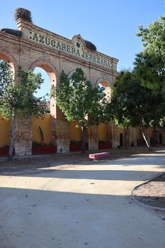 Sunlit historic Azucarera Jerezana brick arches surrounded by trees in El Portal, Spain.
