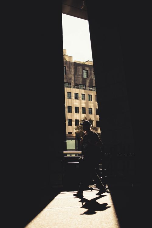 Free A silhouetted person walking through a city street, framed by modern architecture in dramatic lighting. Stock Photo