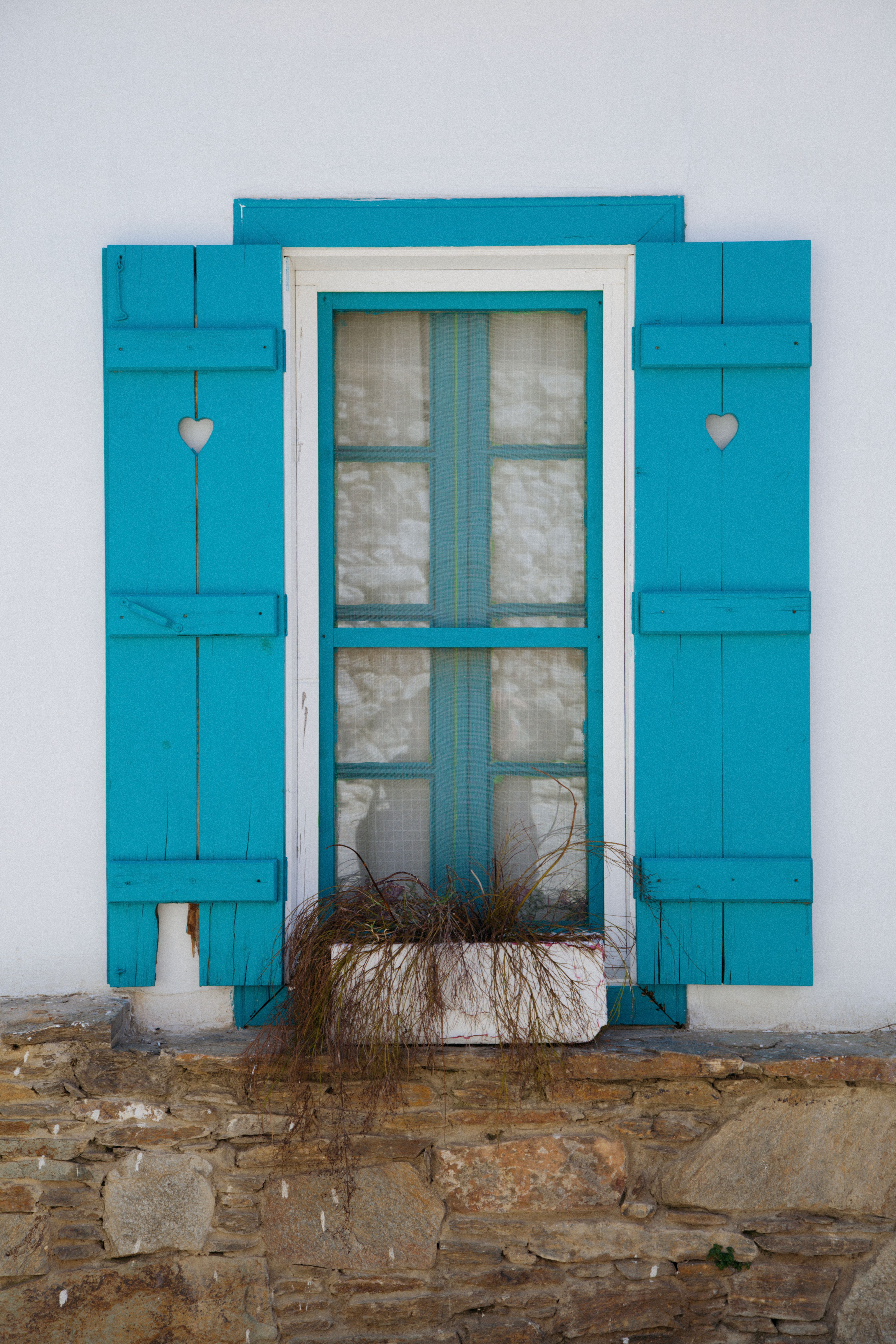 Blue shuttered window with heart cutouts, stone wall, and planter box.
