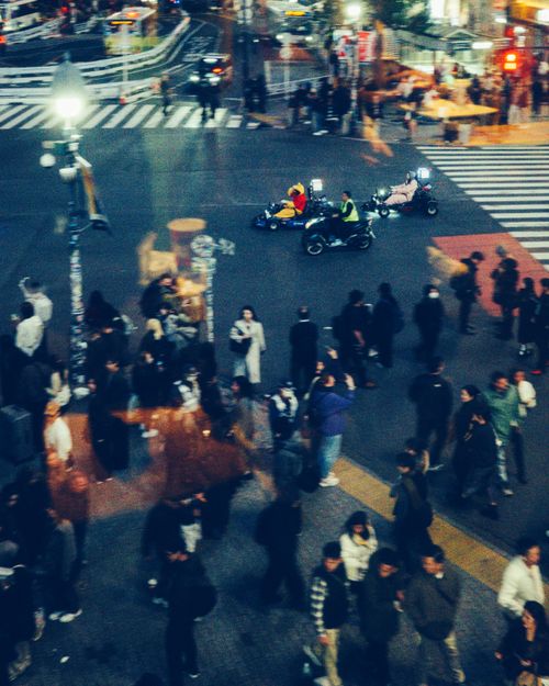 Free Dynamic Tokyo street crossing at night with go-karts and bustling crowd. Stock Photo