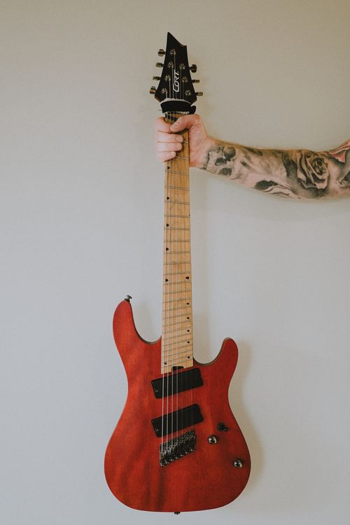 Free Close-up of tattooed arm holding a sleek red electric guitar with a minimalist background. Stock Photo