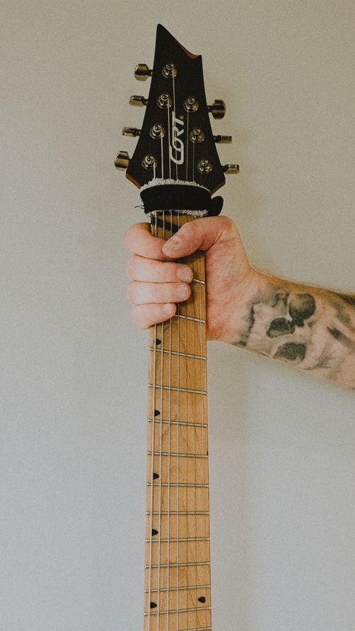 Free Close-up of a tattooed hand holding the neck of a guitar, focusing on the detailed fretwork. Stock Photo