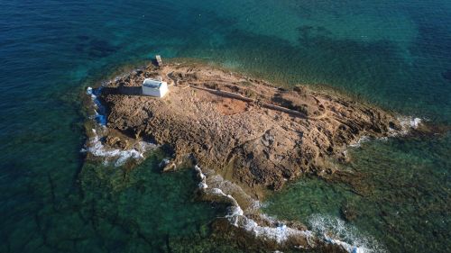 Free Aerial shot of a small rocky island with a white building near Malia, Greece. Stock Photo