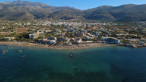 Free Stunning aerial photo showcasing the beach and town of Malia, Crete, Greece with mountainous backdrop. Stock Photo
