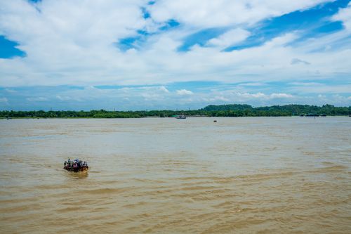 Free Wide river scene with a small boat under a blue sky, lush green landscape in the background. Stock Photo