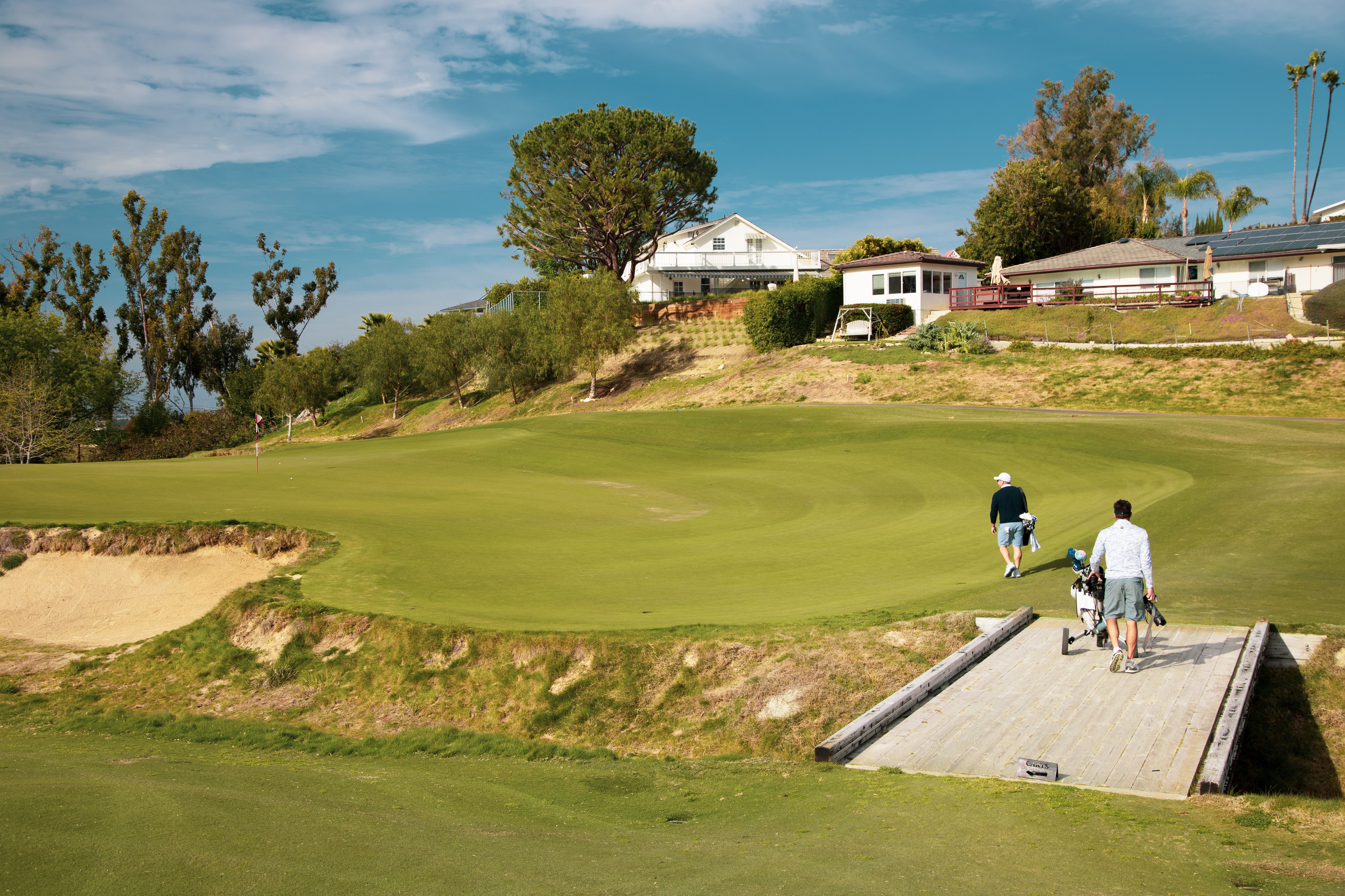 Two golfers walking on a sunny golf course in Los Angeles, California, with lush greenery and clear skies.