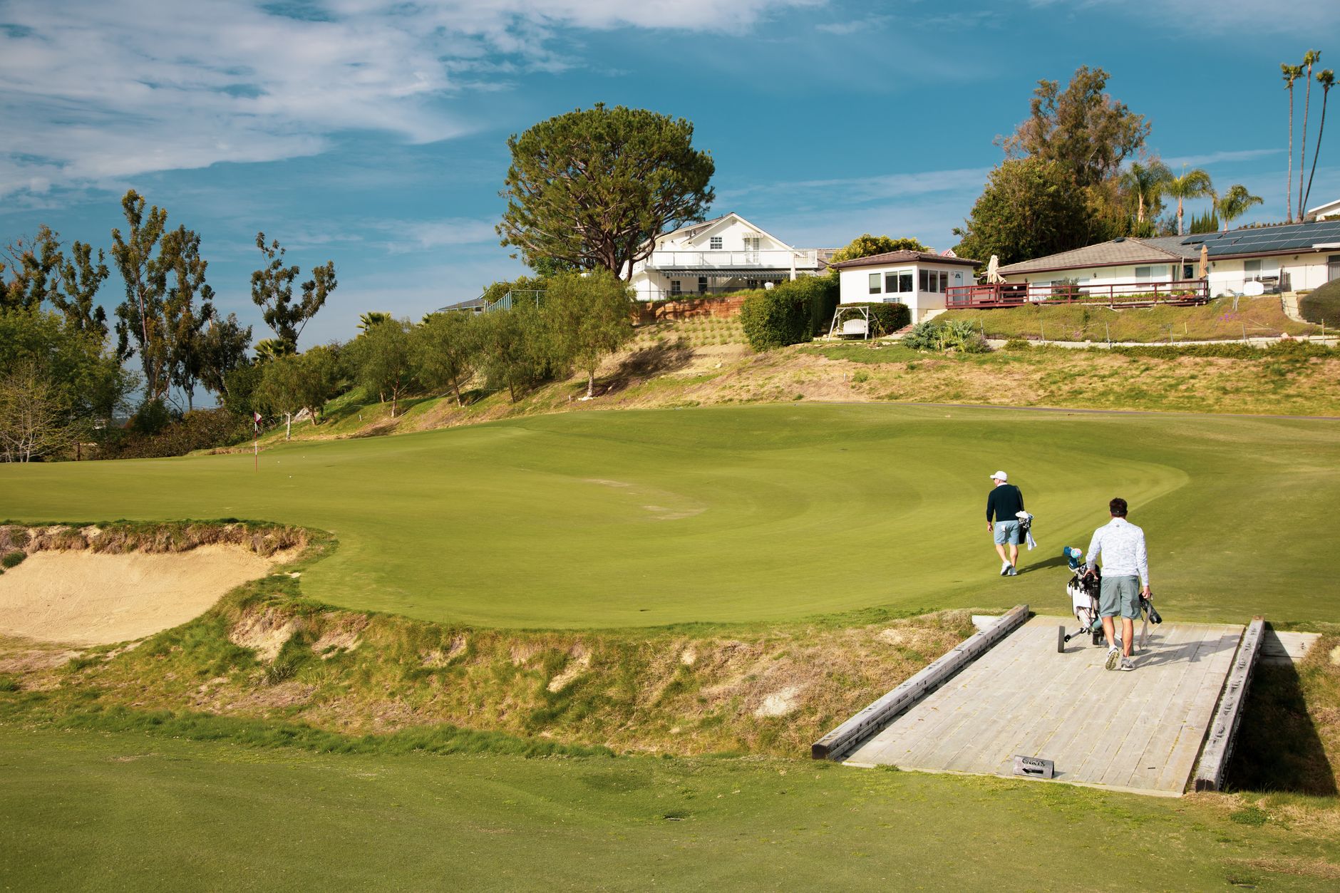 Two golfers walking on a sunny golf course in Los Angeles, California, with lush greenery and clear skies.