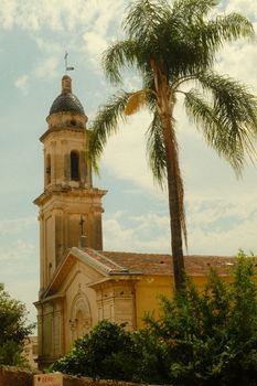 A vintage view of a historic church beside a palm tree in the French region of Provence.