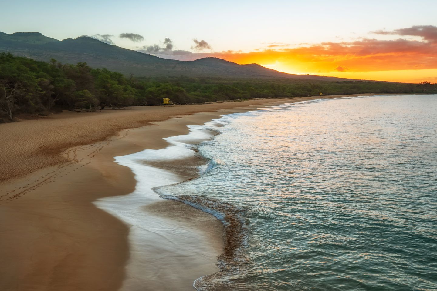 A sunset shoreline with waves running up dark sand