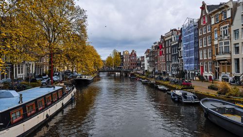 Free Picturesque Amsterdam canal scene featuring colorful autumn leaves and classic architecture. Stock Photo