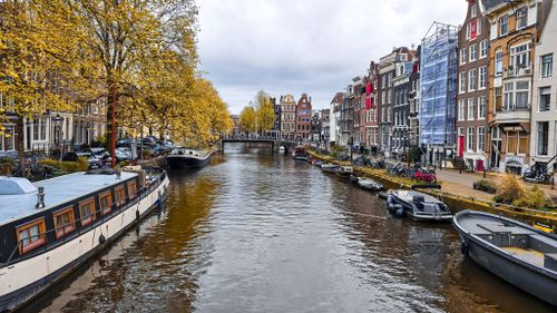 Free Explore the picturesque Amsterdam canal lined with historic buildings and autumn trees. Stock Photo