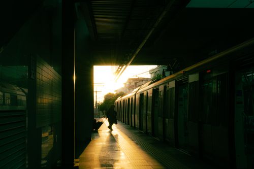 Free A silhouetted person waits at a dimly lit train station platform during a stunning sunset. Stock Photo