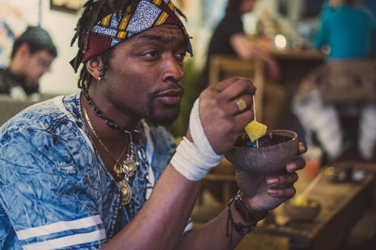 Crop Serious Black Man Eating Pineapple Slices In Street Cafe