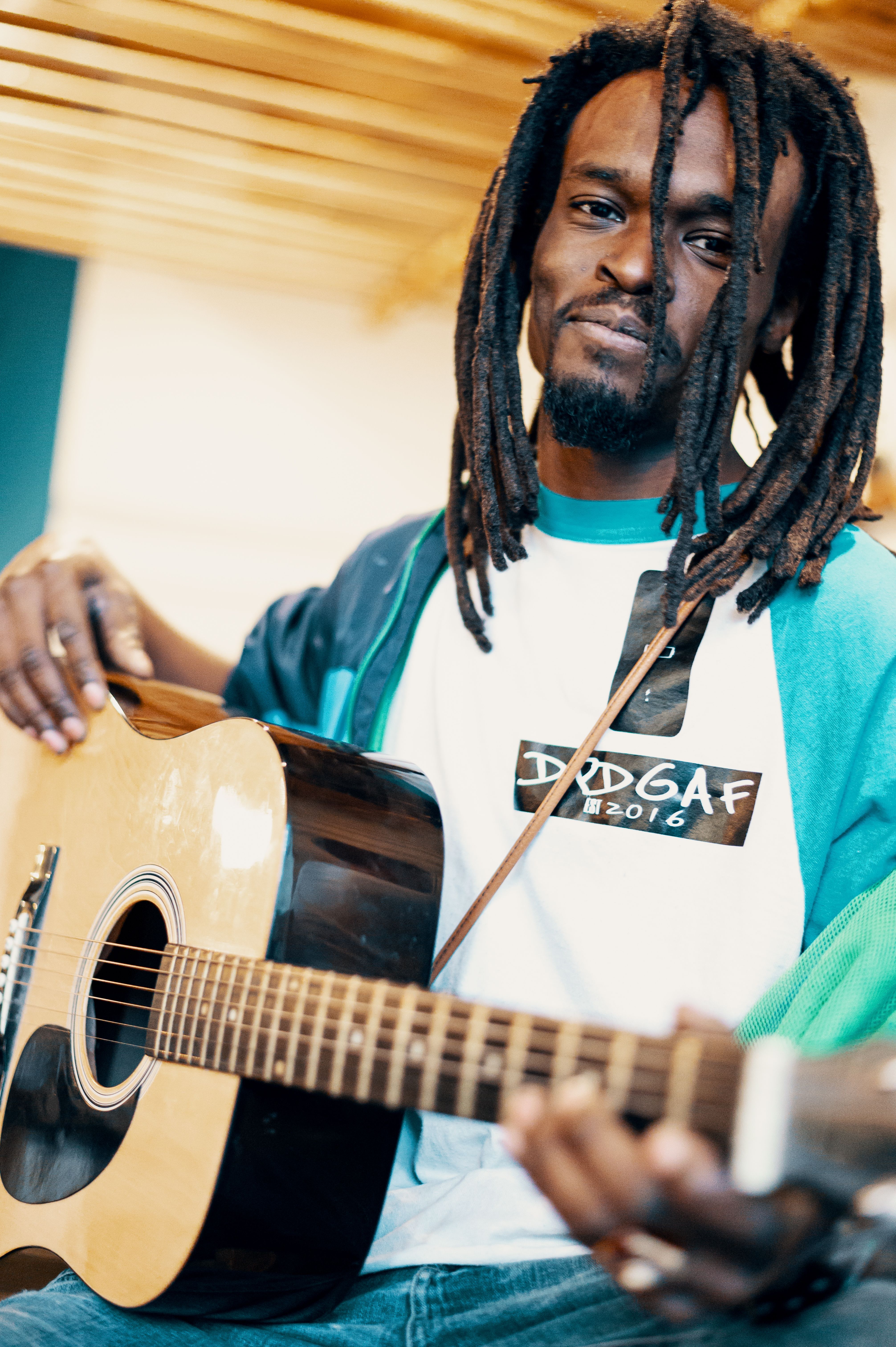 Portrait of a black man with dreadlocks playing an acoustic guitar indoors.