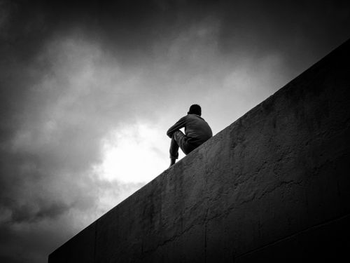 Free Silhouette of a man sitting on a wall against a cloudy sky, evoking solitude. Stock Photo