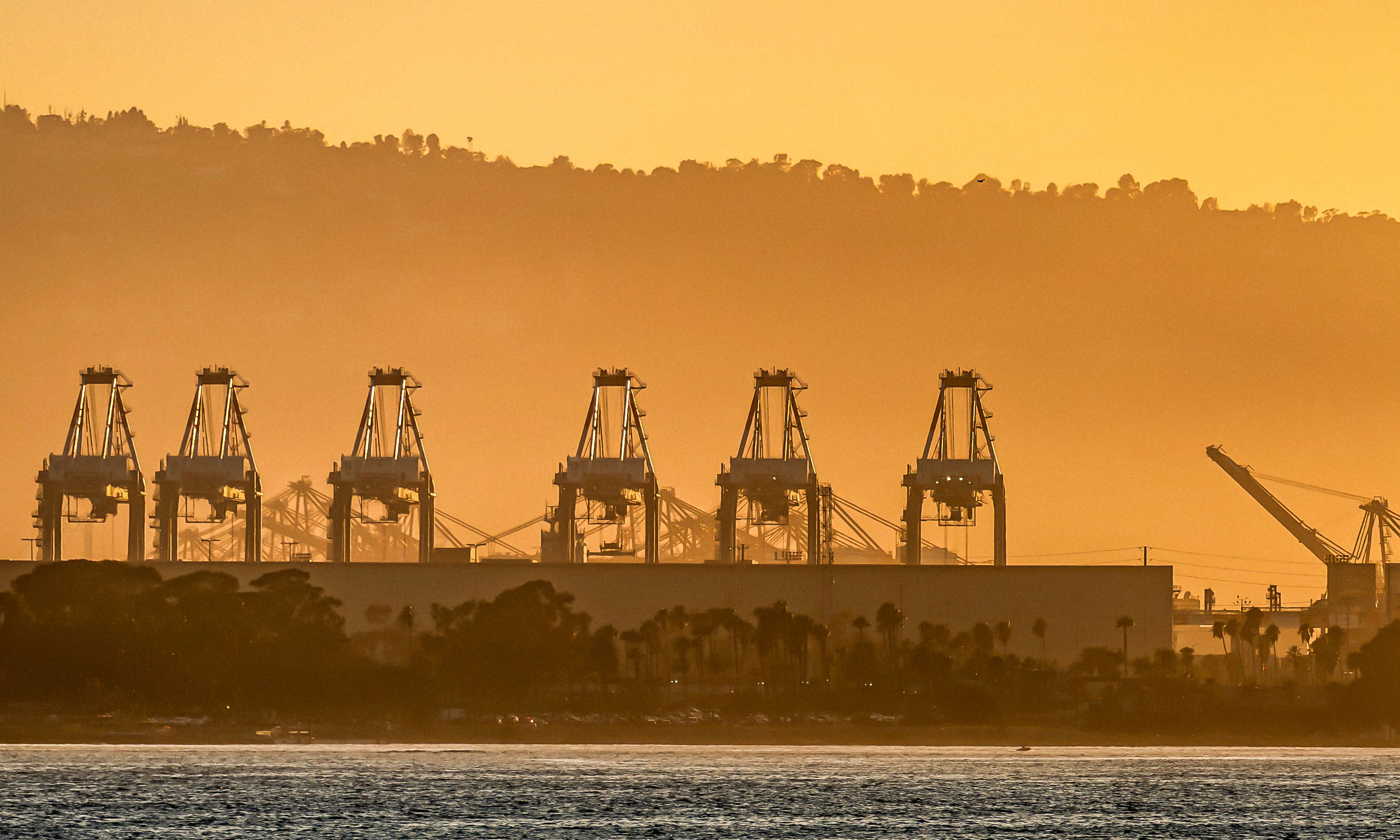 Silhouetted cargo cranes at sunset in a seaport, capturing industrial elegance.