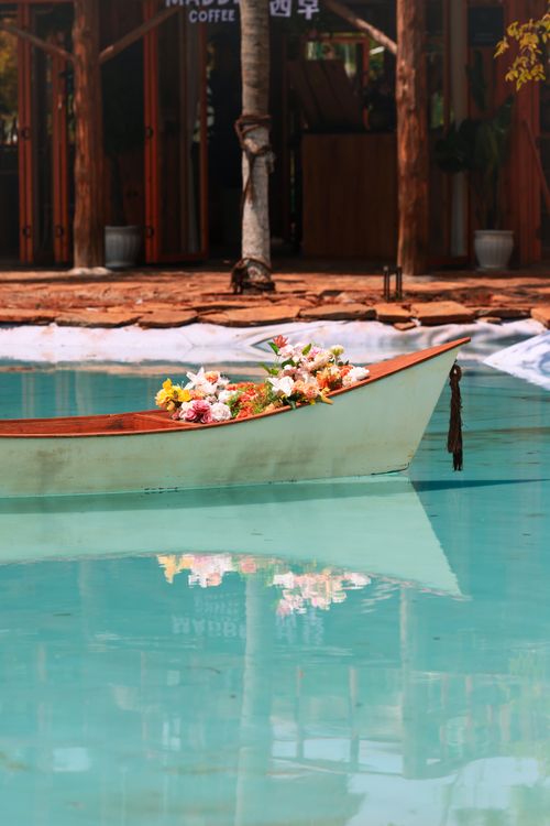 Free A beautiful boat filled with vibrant flowers floating on a serene pool reflecting tranquility. Stock Photo