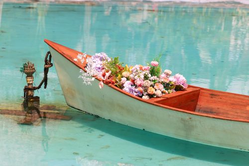 Free A serene wooden boat filled with vibrant flowers floating on clear water, exuding a sense of calm and beauty. Stock Photo
