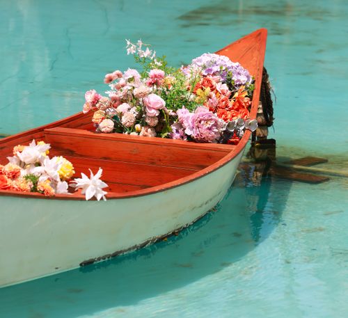 Free A wooden rowboat filled with colorful flowers, floating on calm turquoise water, capturing a serene, summer scene. Stock Photo